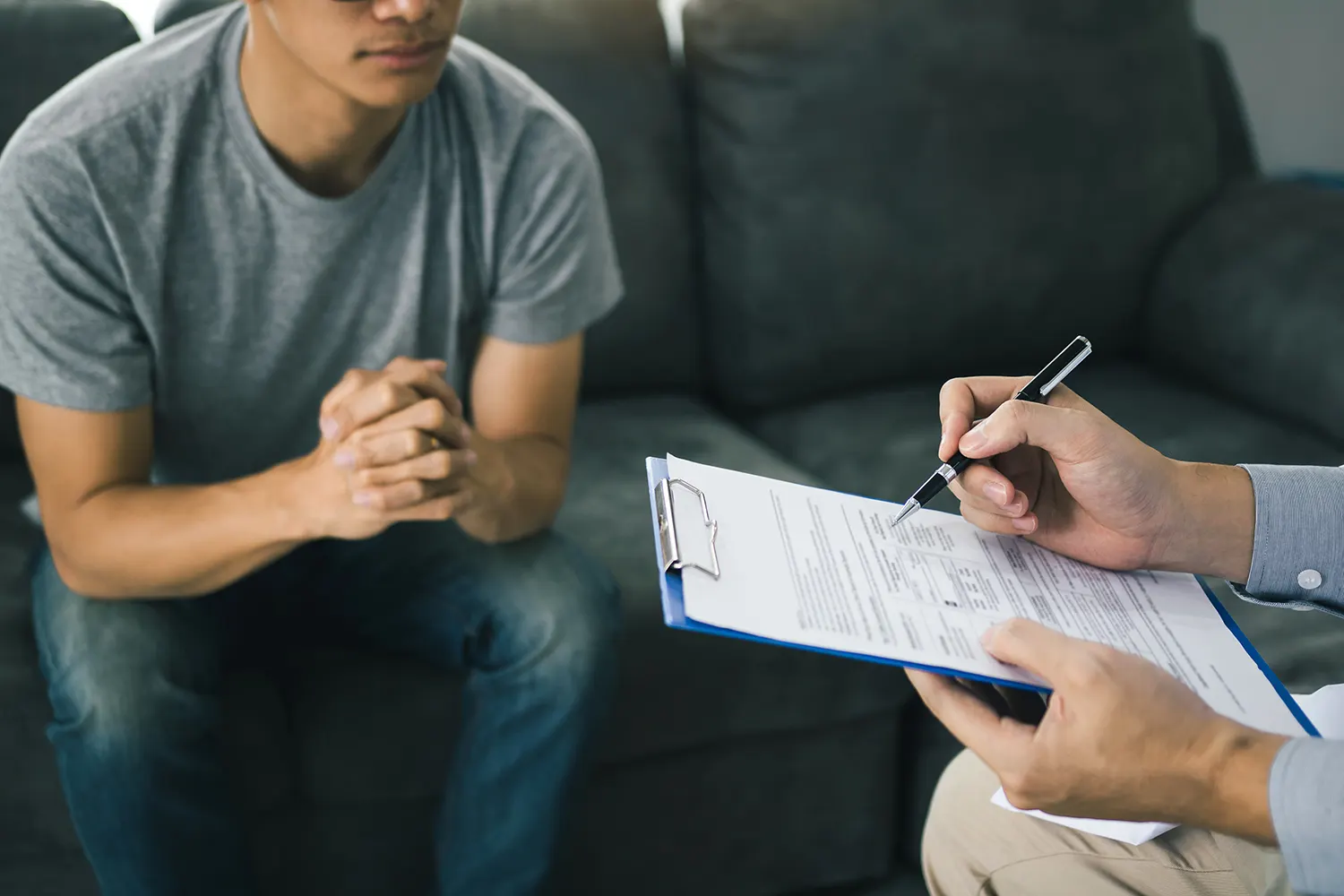 Patient on a couch while a staff member fills out an intake form on a clipboard