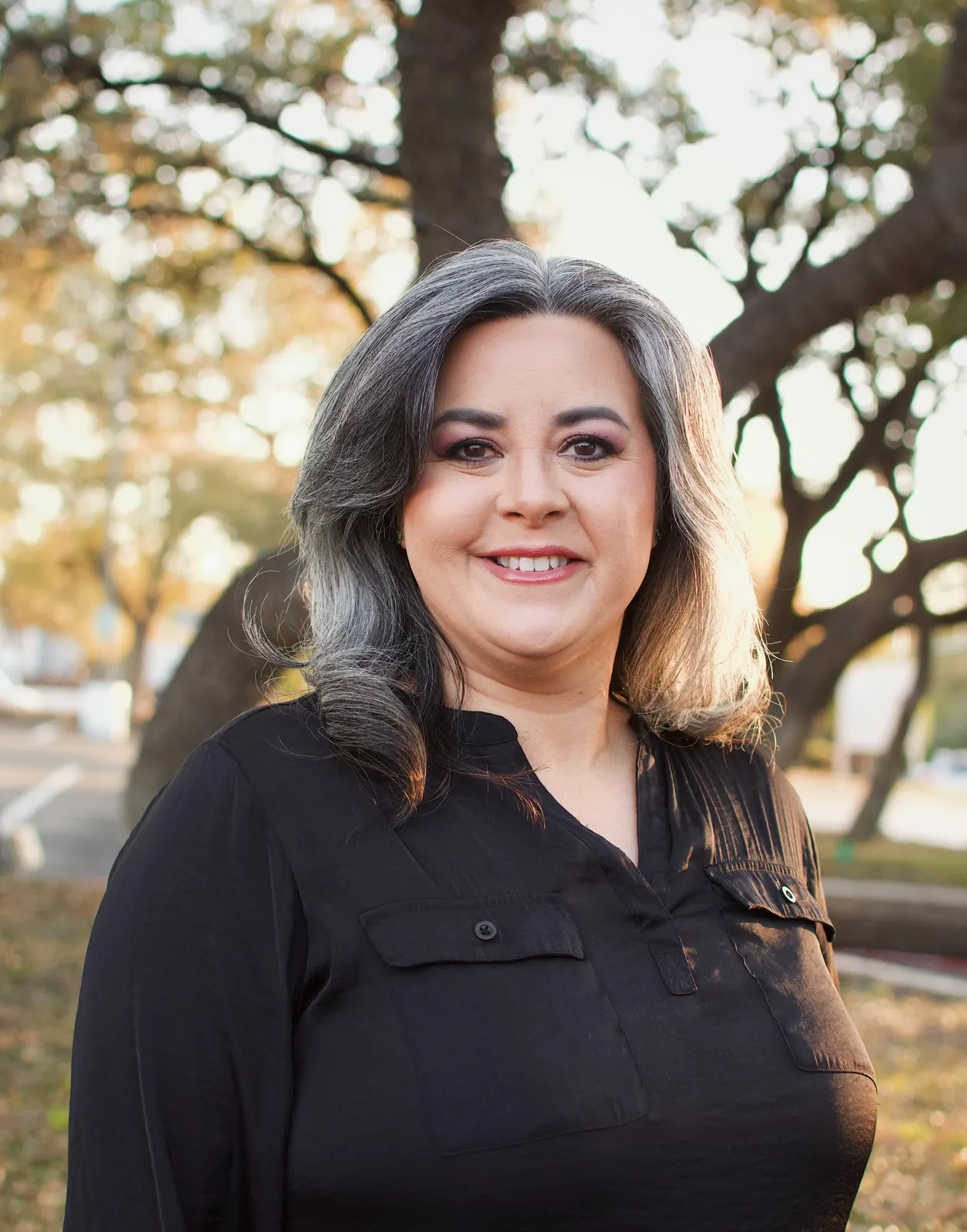 Nicole, Office Manager at Castle Hills Chiropractic, standing outdoors under a tree